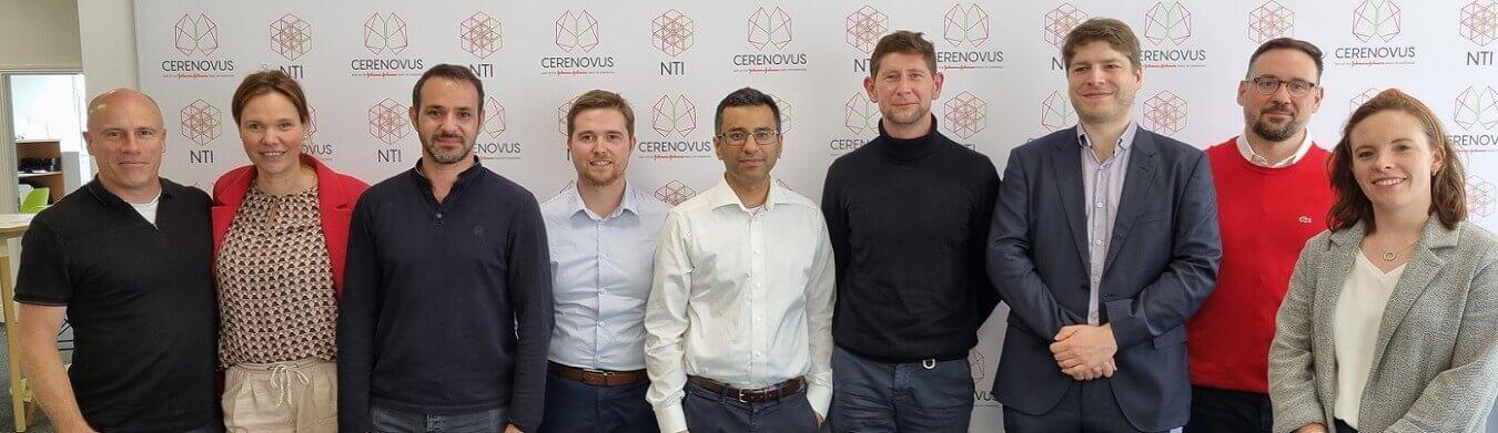 Mahmood Mirza in the center of 8 colleagues in front of a CERENOVUS NTI branded background.